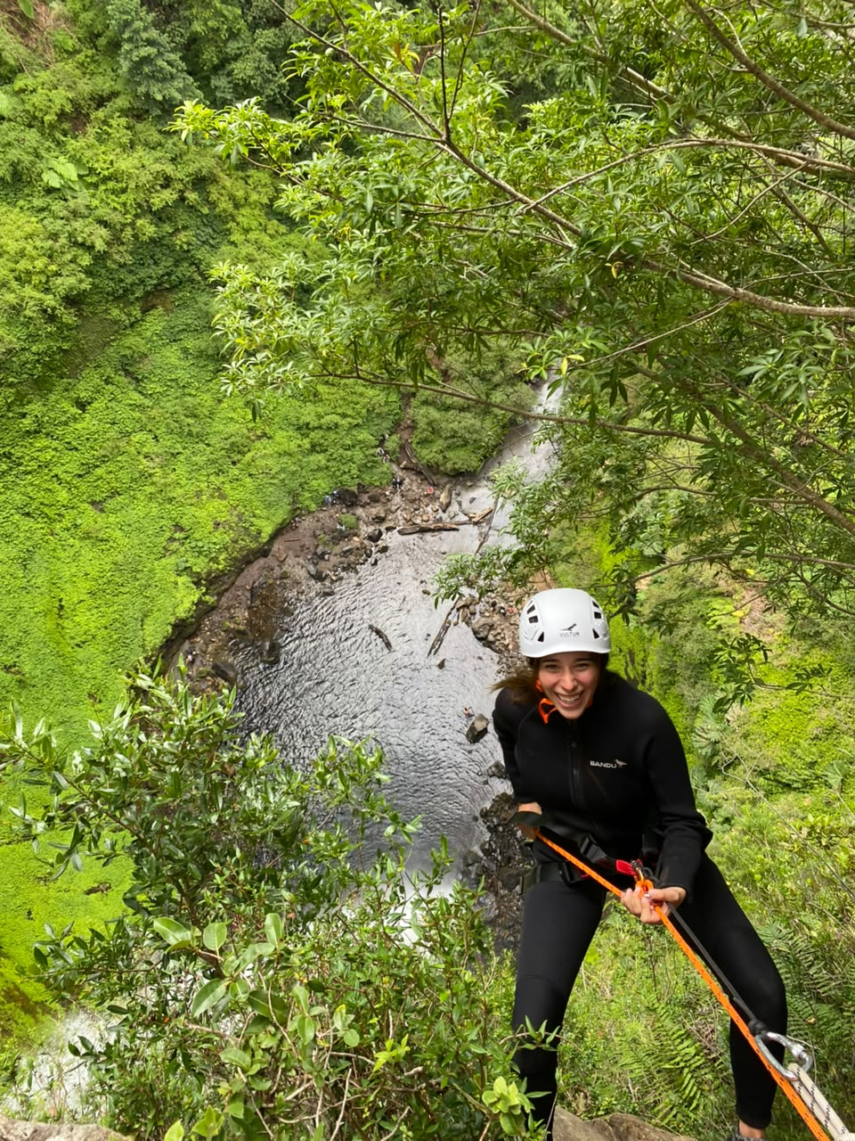 Participante sonriendo mientras desciende en rápel con el cañón y el río al fondo