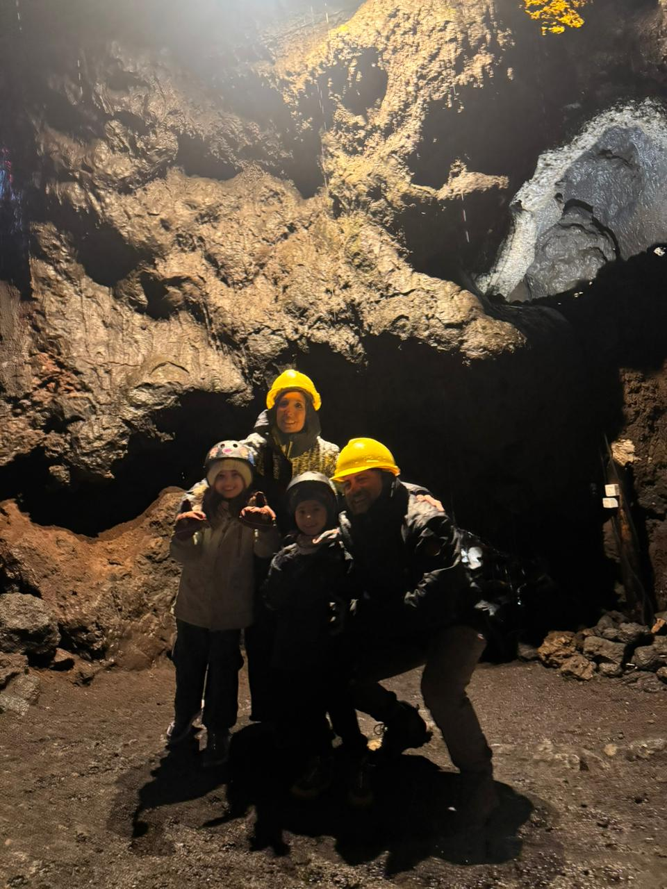 Familia con cascos posando bajo la bóveda de lava iluminada de las cuevas volcánicas