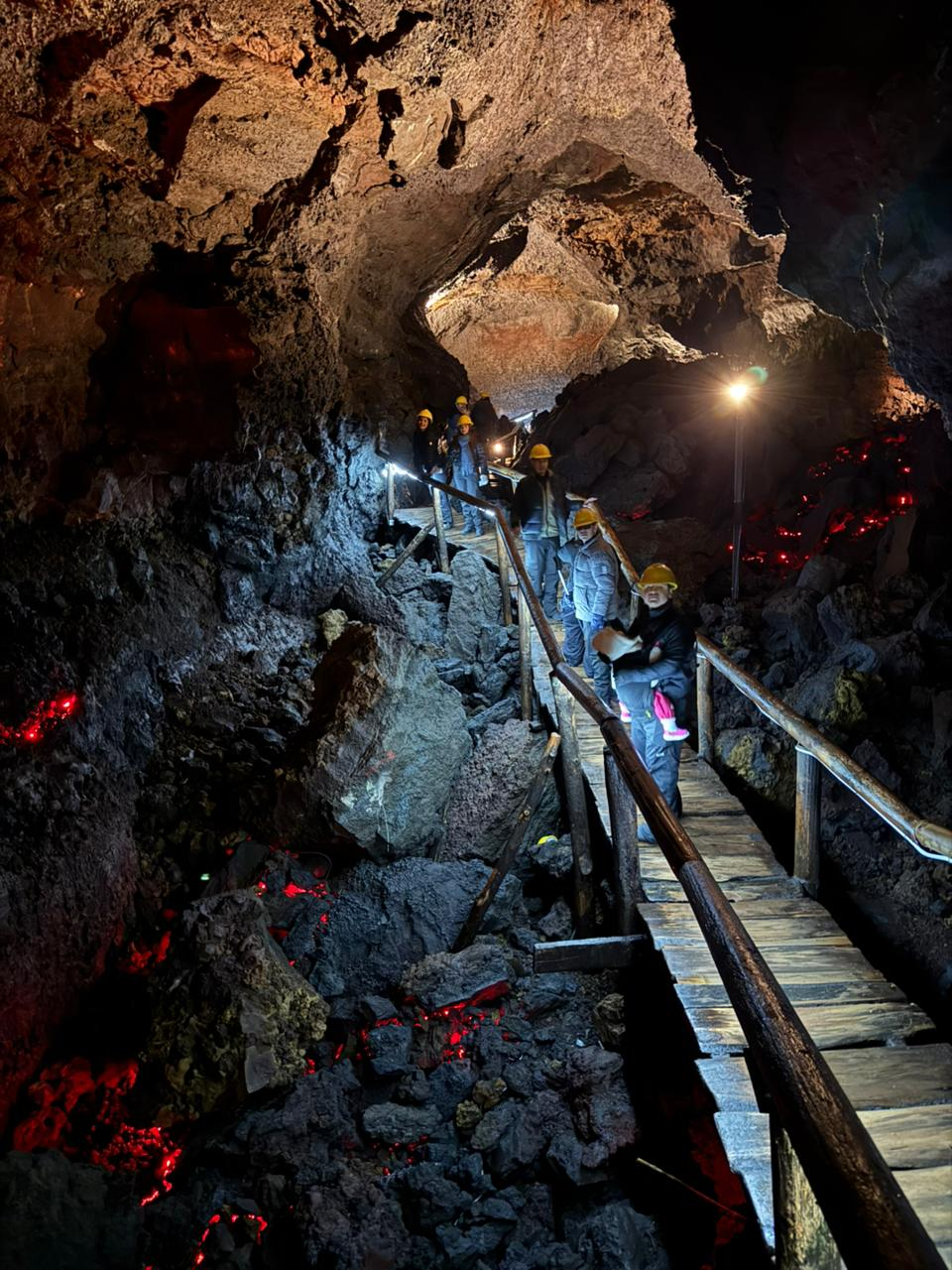 Grupo con cascos amarillos descendiendo por la pasarela de madera de un túnel de lava iluminado en rojo