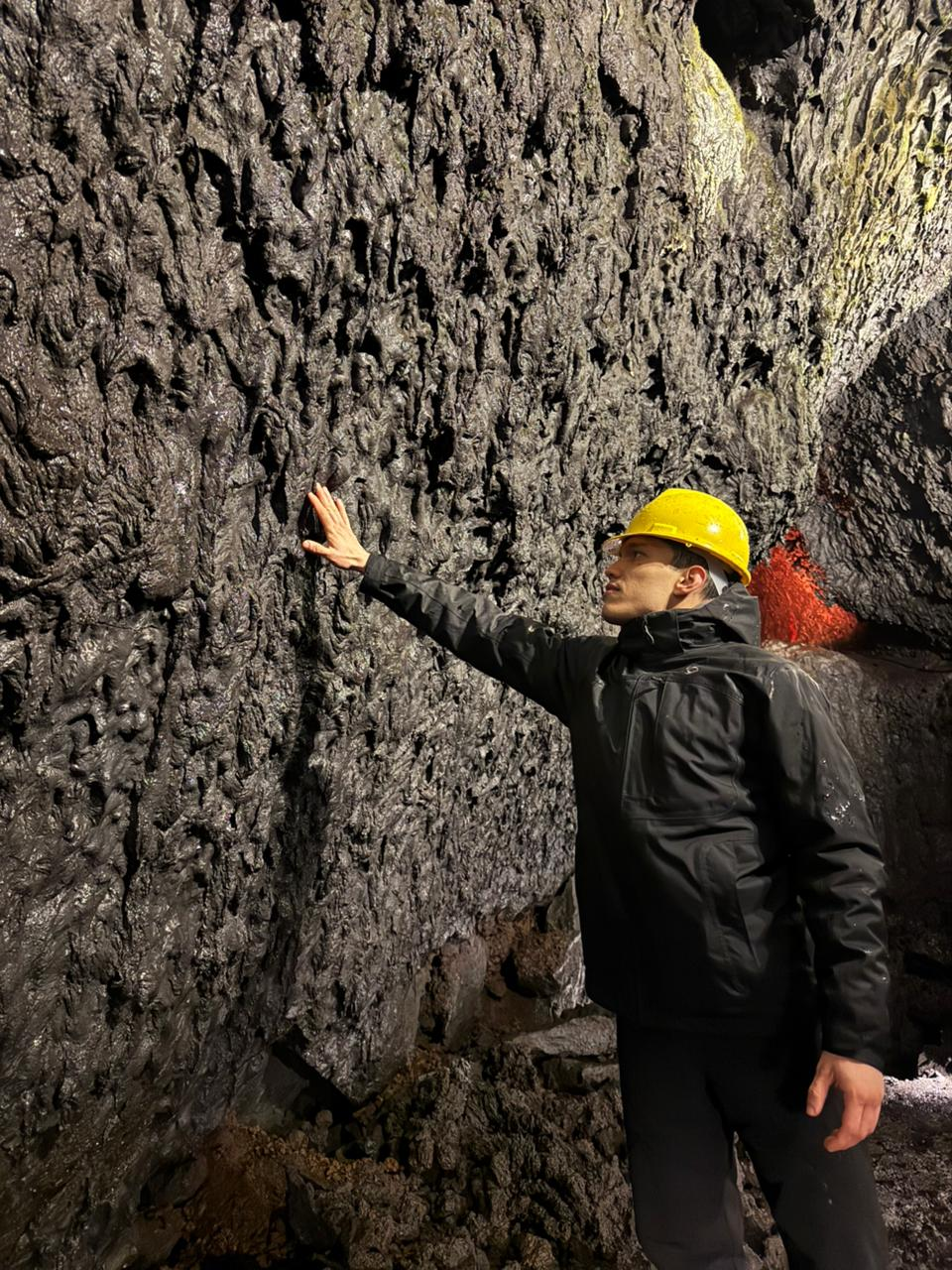 Visitante con casco amarillo tocando la pared de lava petrificada dentro de la cueva volcánica