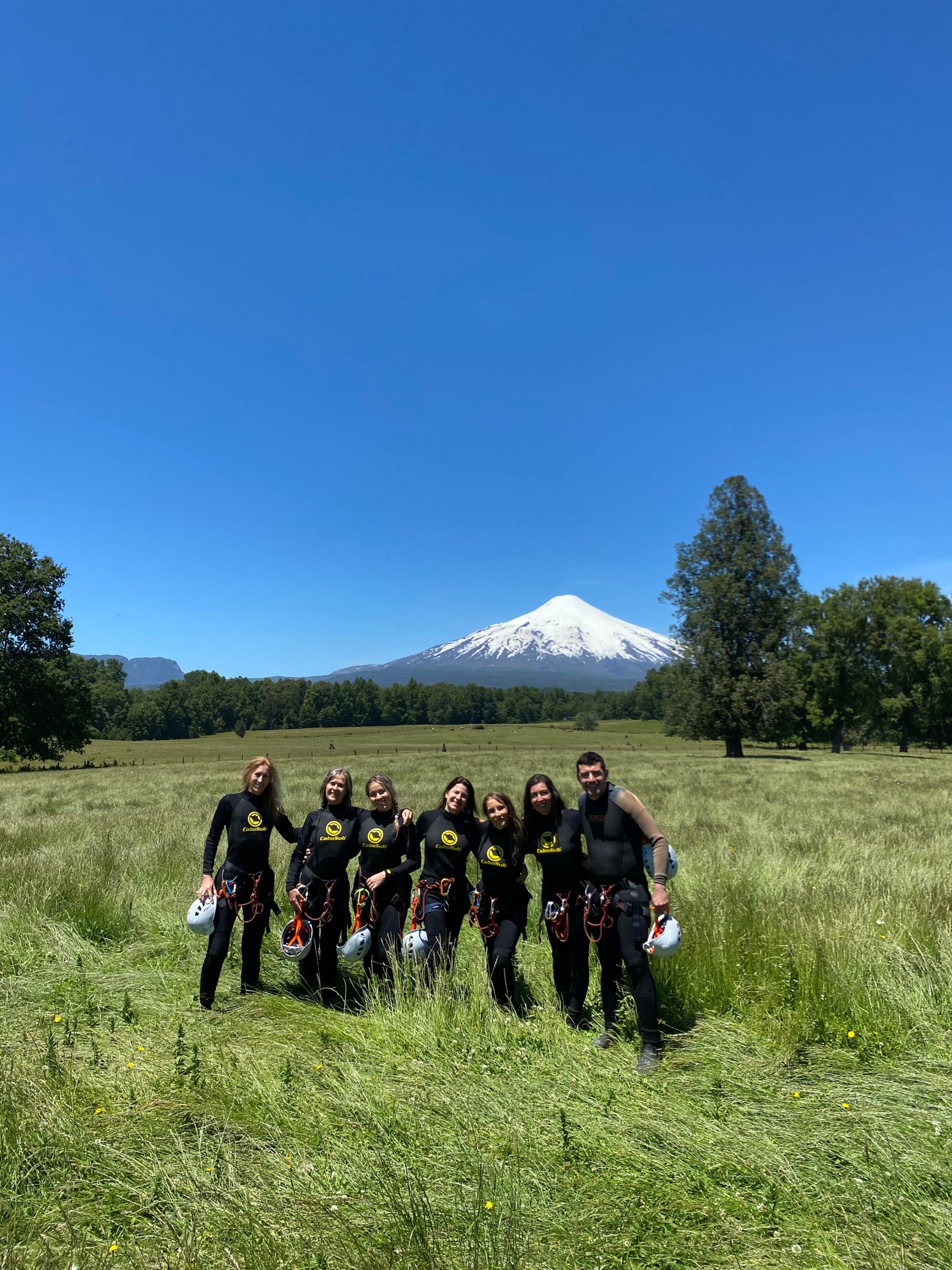 Grupo de Vultur Expediciones con trajes de neopreno en una pradera con el Volcán Villarrica al fondo