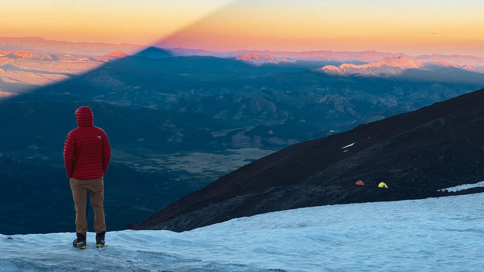 Montañista en la nieve del Villarrica al amanecer, con la sombra del volcán sobre el valle