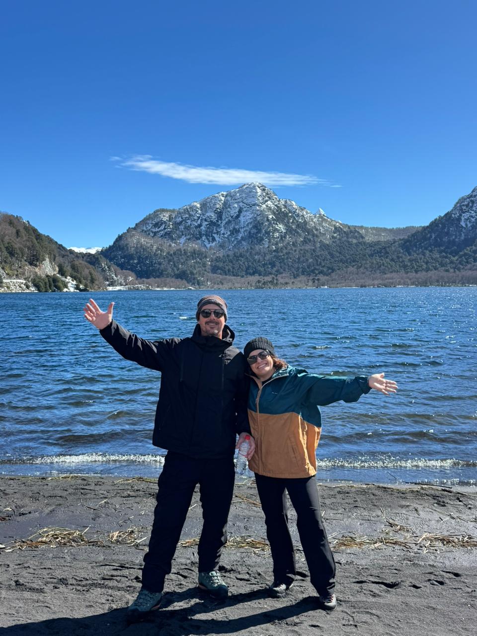 Pareja celebrando en la orilla de la laguna con los cerros nevados detrás