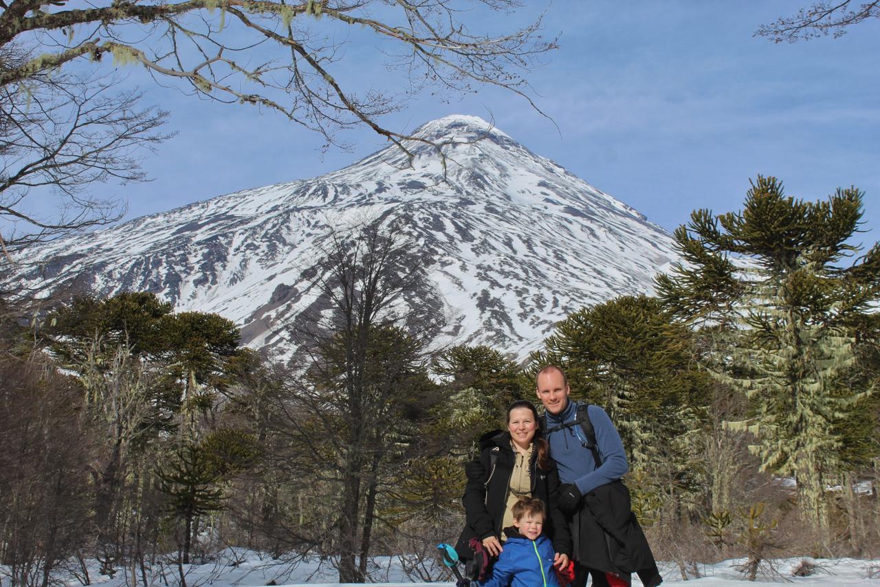 Familia mirando a la cámara en la nieve del sendero, con el volcán Lanín y las araucarias de fondo
