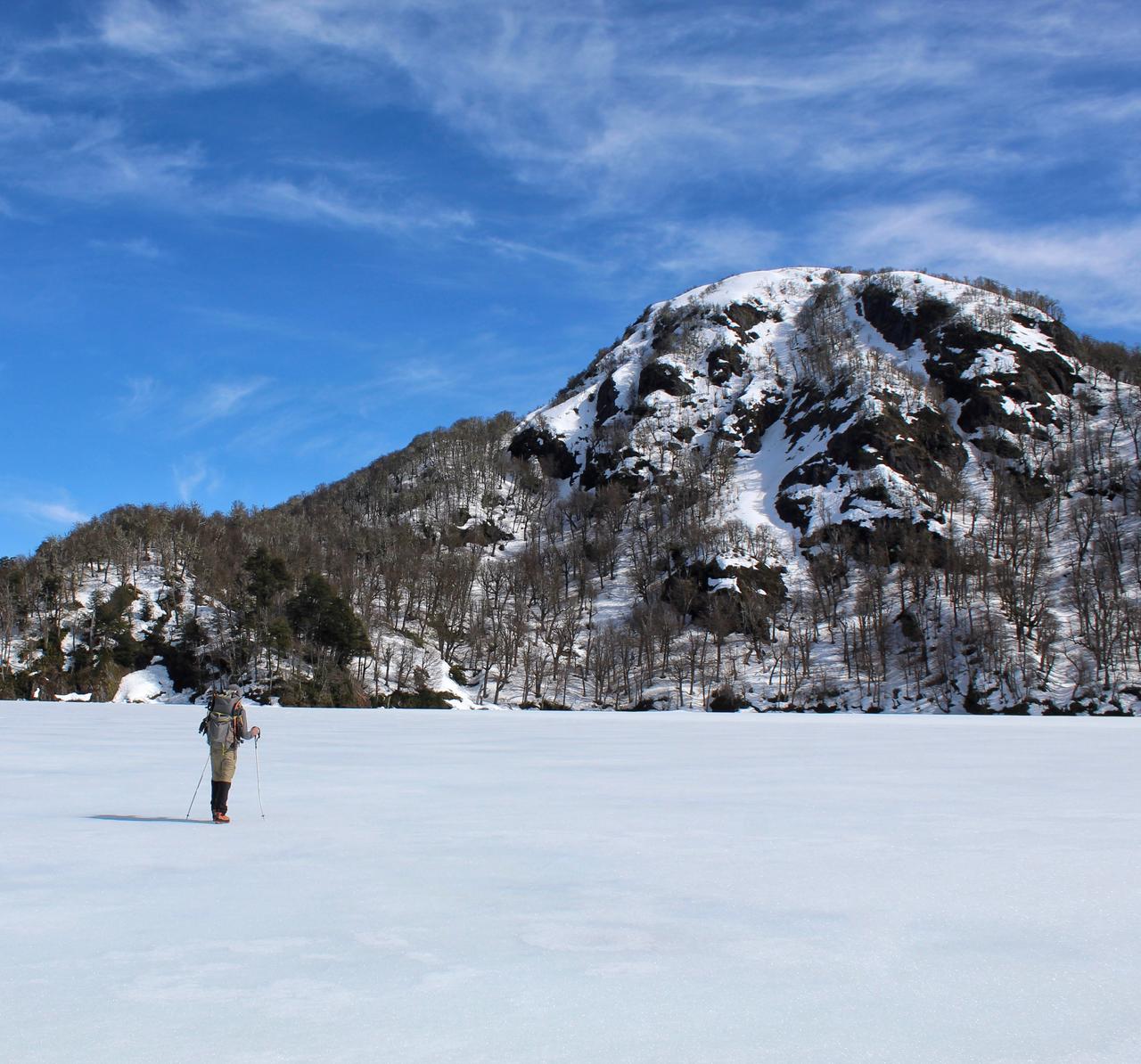 Caminante solitario cruzando una laguna congelada al pie de un cerro nevado