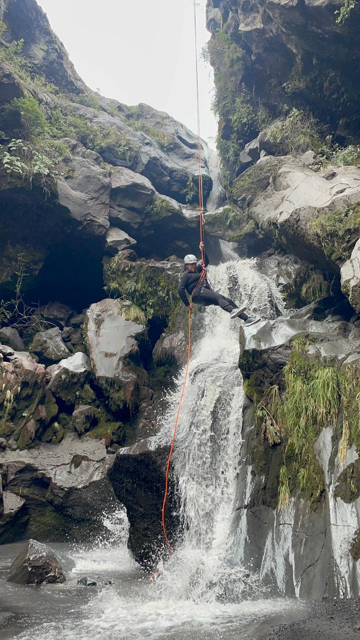 Participante descendiendo en rápel por una cascada del cañón El Pillán entre paredes de roca volcánica