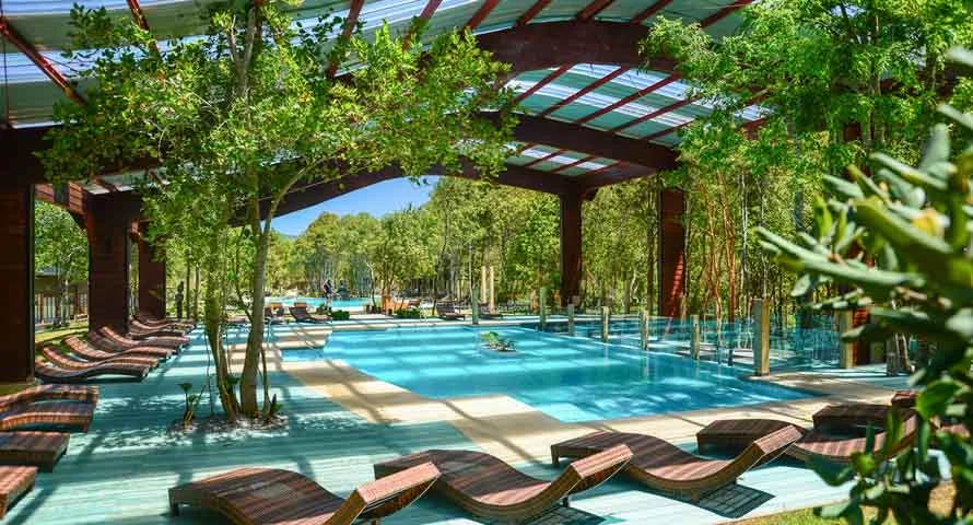 Piscina termal turquesa bajo una pérgola de madera con reposeras entre los árboles